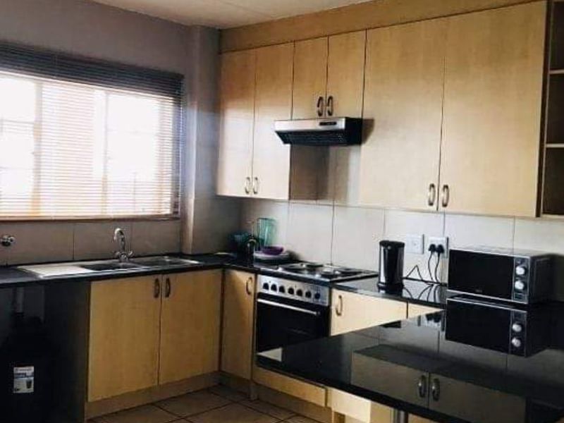 Functional kitchen featuring light wood cabinetry, black granite countertops, tiled flooring, and integrated cooking appliances including an oven and extractor fan.