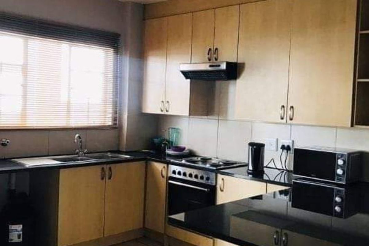 Functional kitchen featuring light wood cabinetry, black granite countertops, tiled flooring, and integrated cooking appliances including an oven and extractor fan.