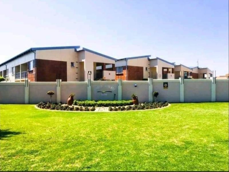 Front view of a well-maintained residential complex featuring a landscaped garden, perimeter wall with electric fencing, and modern multi-unit building architecture.