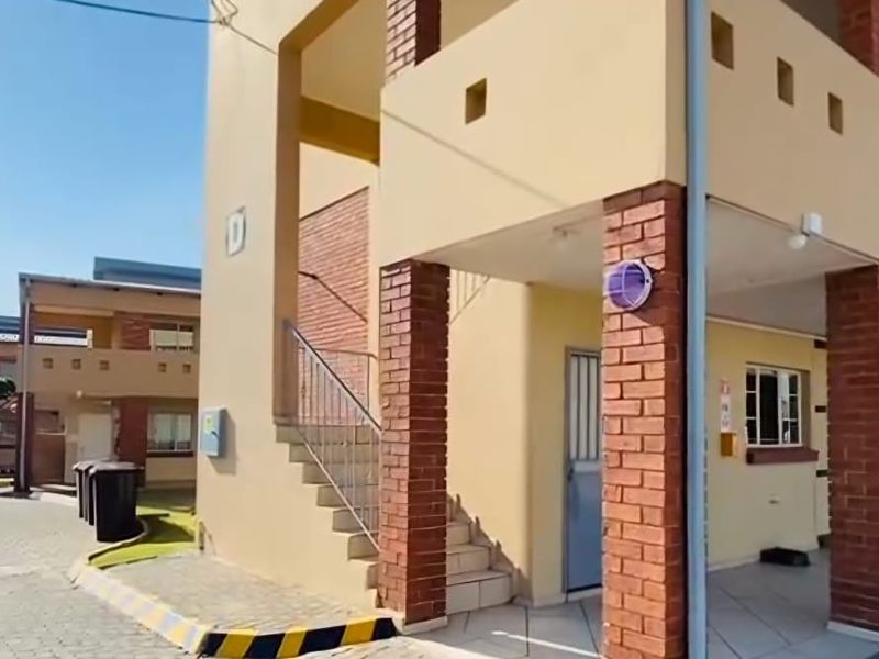 Exterior view of a commercial building complex featuring brick pillar accents, an external staircase, and paved driveway access.