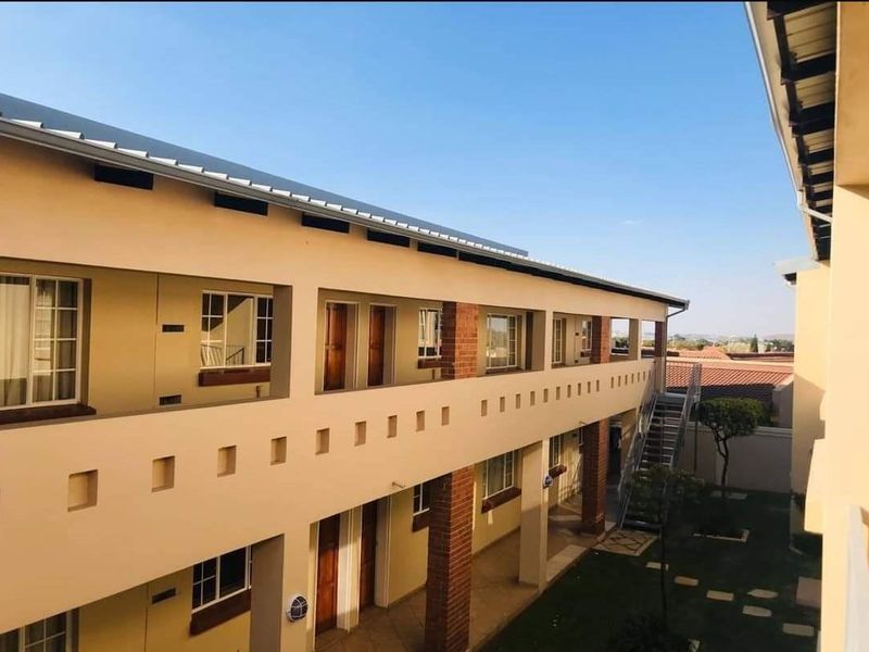Exterior view of a multi-story commercial or residential complex featuring a balcony walkway, brick support pillars, and an external metal staircase.