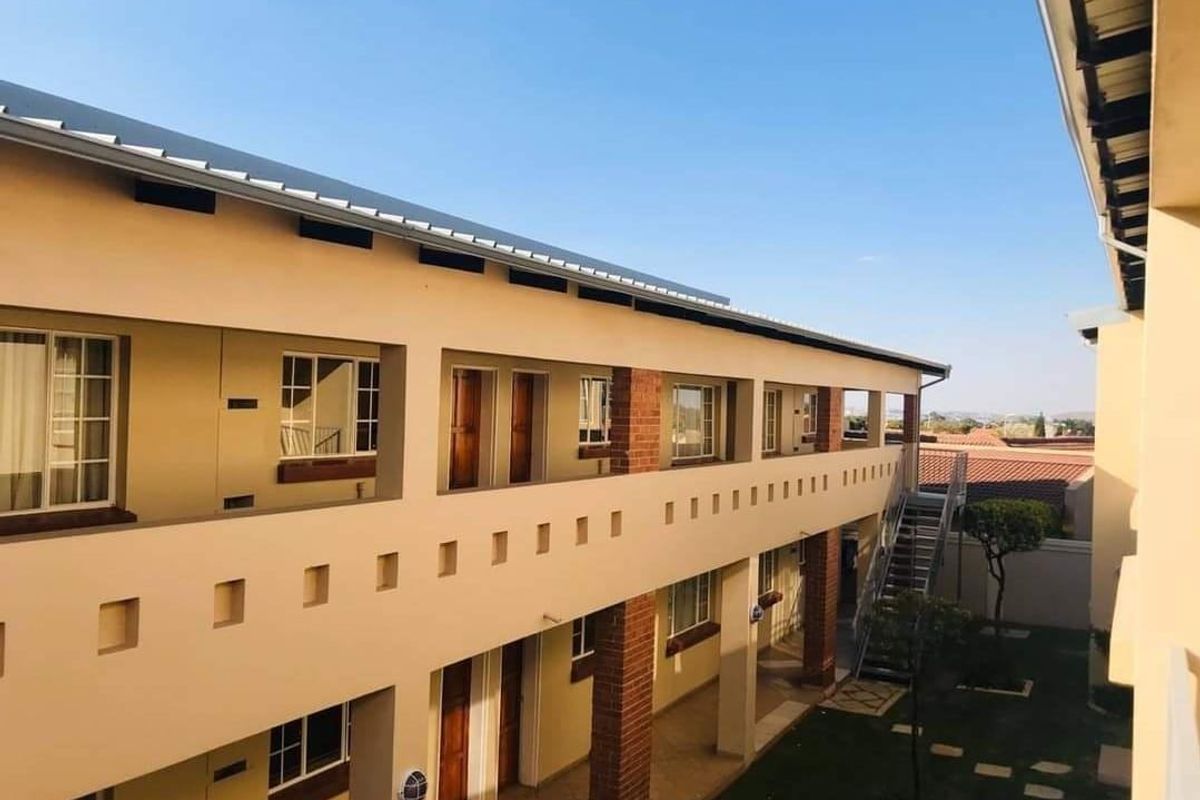 Exterior view of a multi-story commercial or residential complex featuring a balcony walkway, brick support pillars, and an external metal staircase.