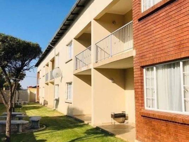 Exterior view of a multi-story commercial building featuring brick masonry, private balconies with metal railings, and ground-level patio access to a landscaped garden area.