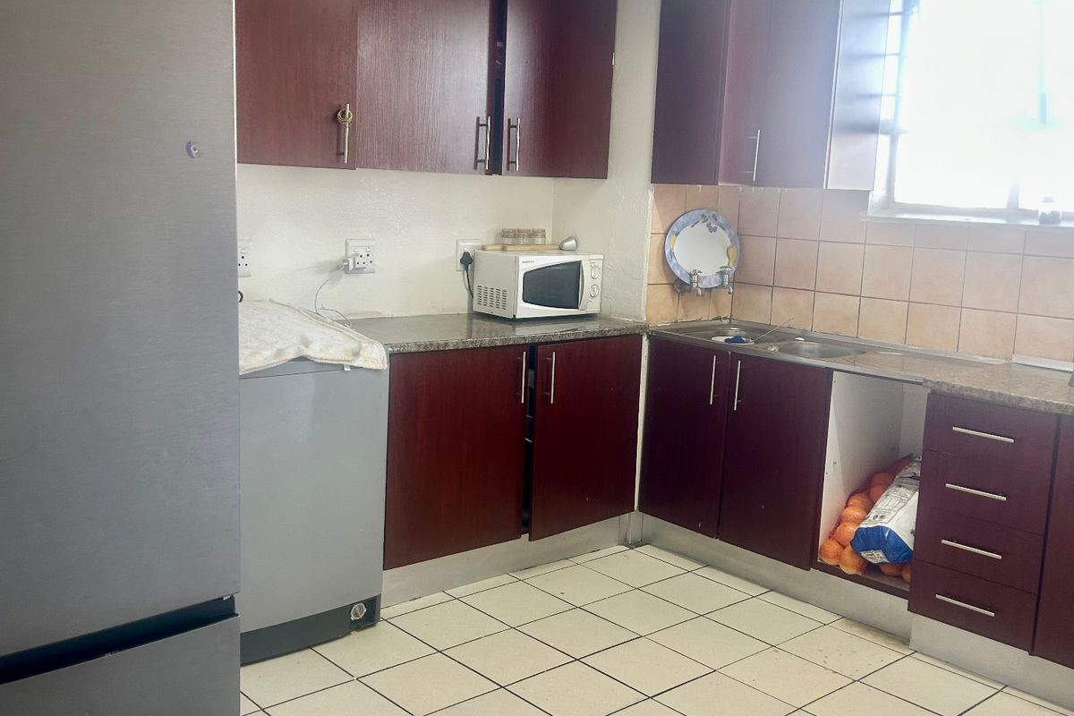 A functional kitchen featuring dark wood cabinetry, granite countertops, and tiled flooring, currently requiring some maintenance and cosmetic updates.