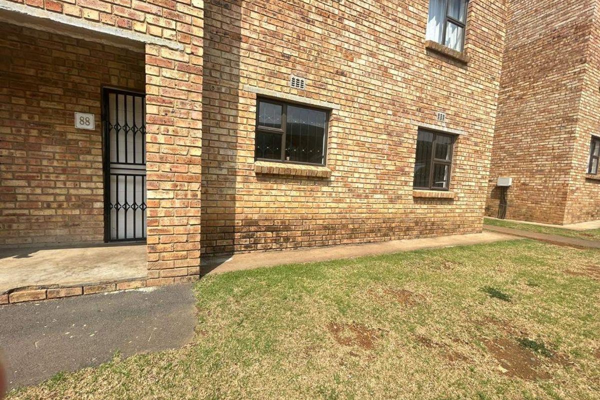 Front exterior view of a face brick townhouse unit featuring a secure entrance gate and aluminium window frames.