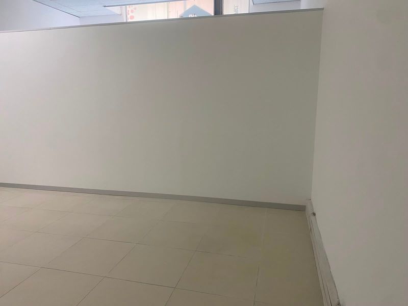 An empty commercial office space featuring neutral tiled flooring, partition walls, and a suspended ceiling, suitable for various business configurations.