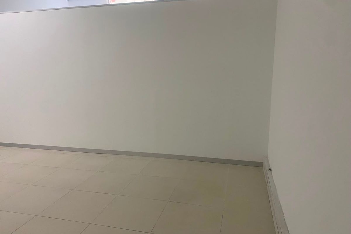 An empty commercial office space featuring neutral tiled flooring, partition walls, and a suspended ceiling, suitable for various business configurations.