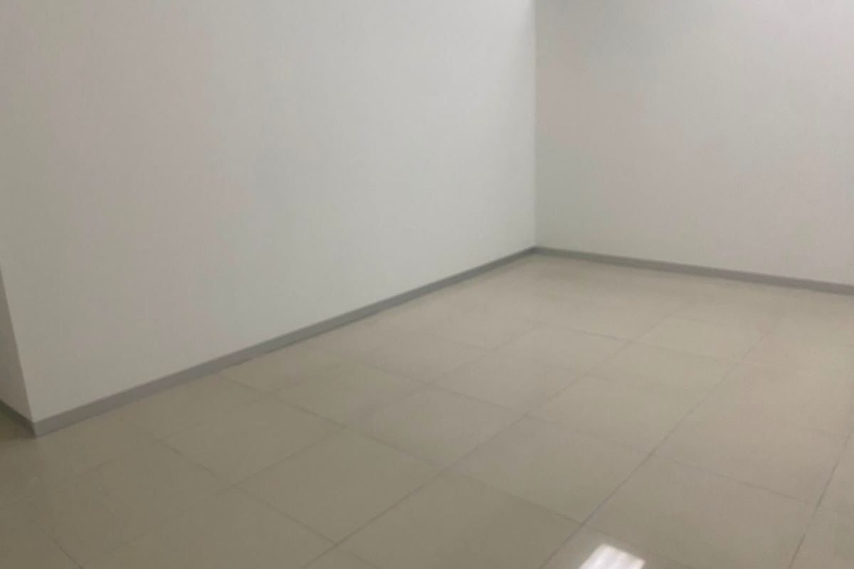 A clean, empty commercial office space featuring neutral tiled flooring and plain white walls, suitable for a variety of business configurations.