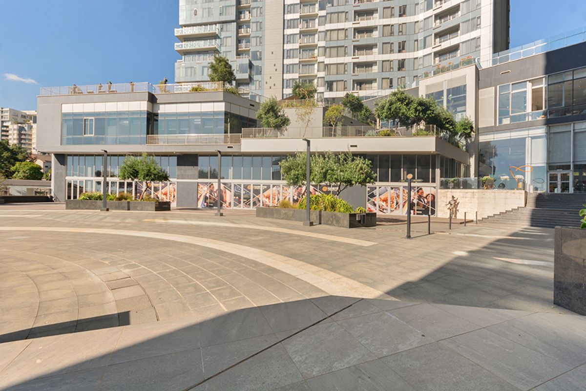A modern commercial plaza featuring paved outdoor space, multi-level terraces, and extensive glass facades on the surrounding building structure.