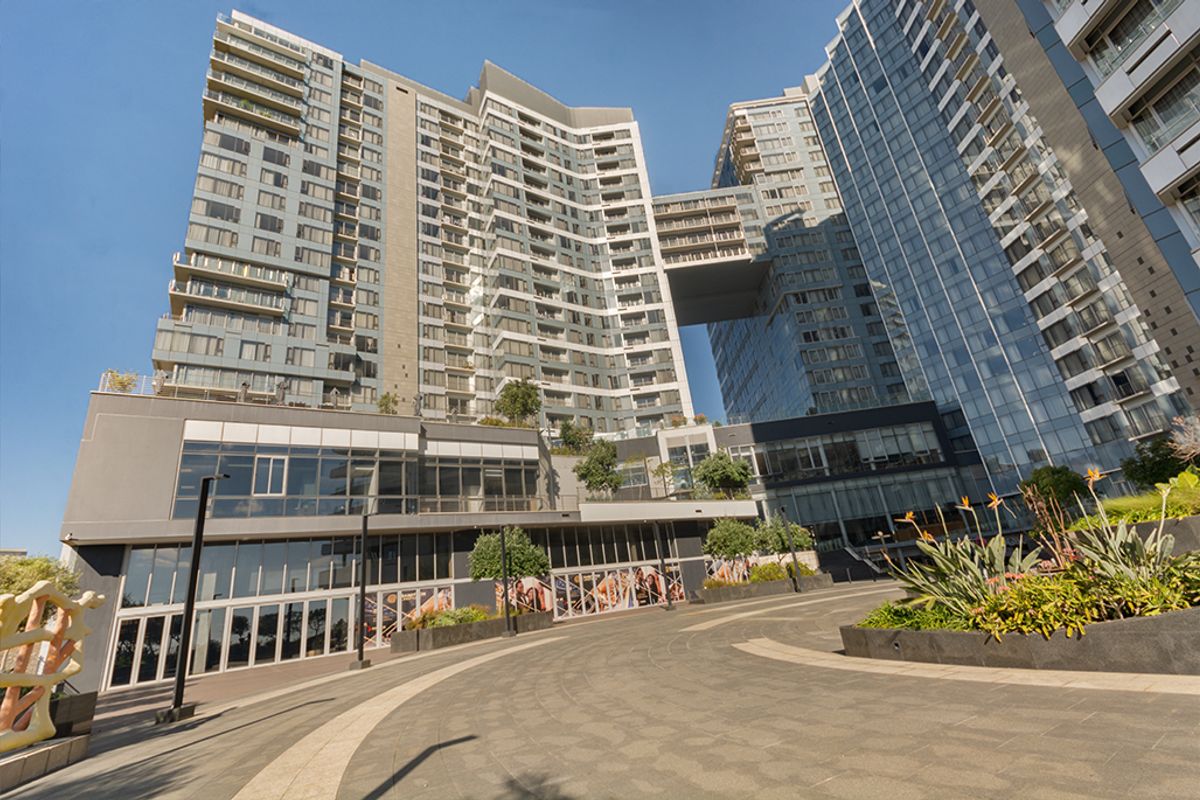 A modern high-rise commercial and residential complex featuring glass facades, integrated balconies, and a paved pedestrian and vehicle approach.
