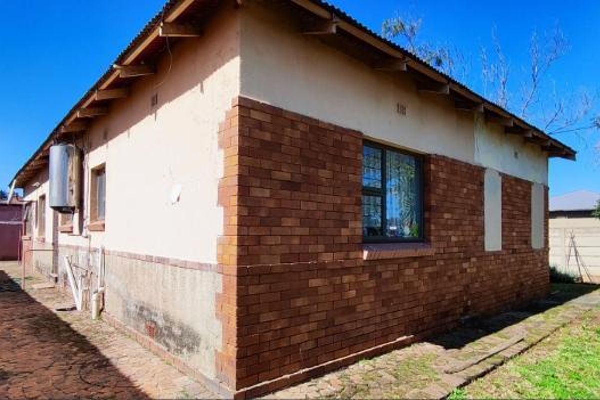 Rear exterior view of the property featuring a brick and plaster facade, external geyser, paved walkway, and surrounding boundary wall.