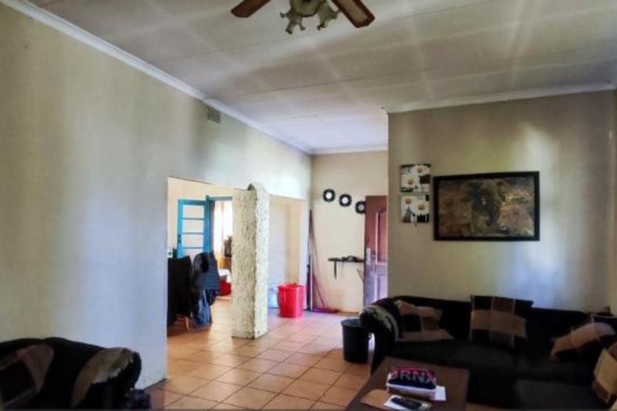 A living room featuring tiled flooring, a ceiling fan, and a textured pillar, leading into an adjacent room.