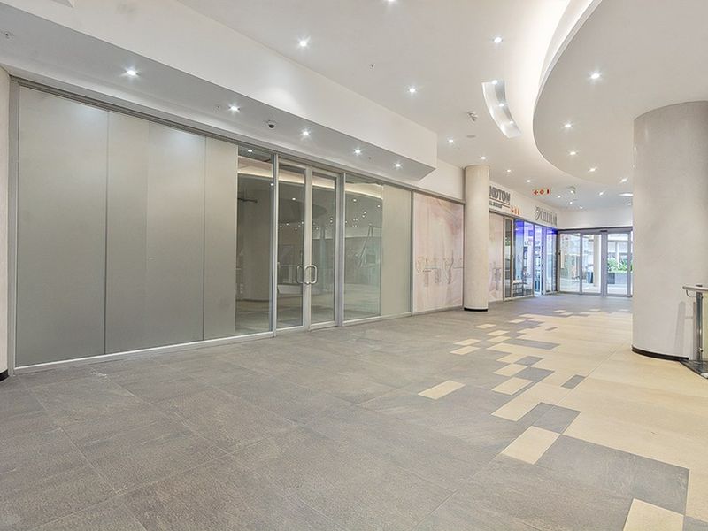 A bright, modern commercial hallway featuring tiled flooring, recessed lighting, and a large glass storefront entrance.