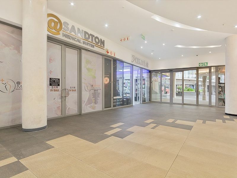 A bright, modern commercial entrance lobby featuring tiled flooring, structural columns, and glass storefronts for medical and retail suites.
