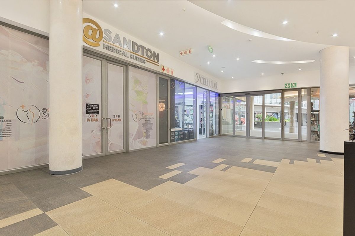 A bright, modern commercial entrance lobby featuring tiled flooring, structural columns, and glass storefronts for medical and retail suites.