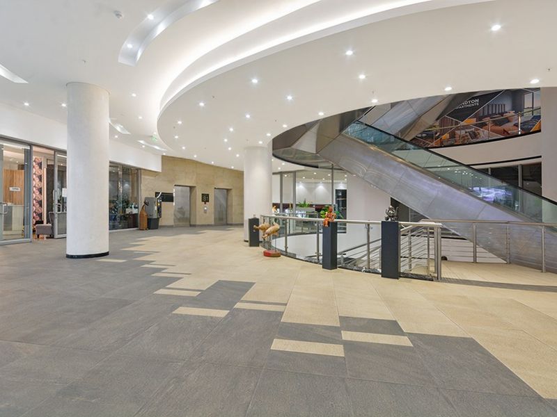 Spacious commercial lobby featuring modern stone flooring, recessed ceiling lighting, and an escalator providing access to lower levels.