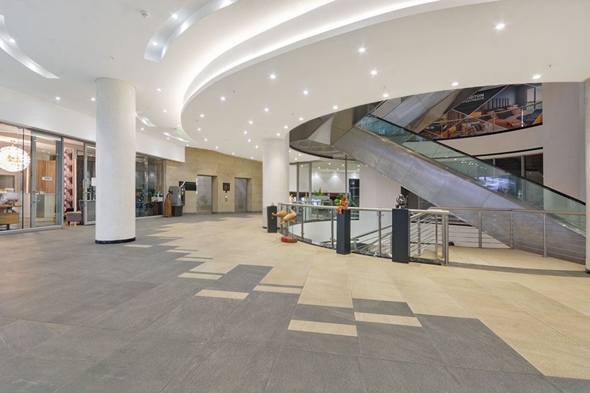 Spacious commercial lobby featuring modern stone flooring, recessed ceiling lighting, and an escalator providing access to lower levels.