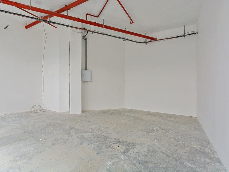 An empty commercial utility space featuring exposed fire sprinkler piping, concrete flooring, and a wall-mounted electrical distribution board.