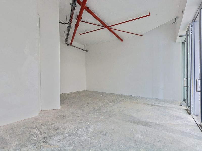 An empty commercial utility space featuring exposed industrial ceiling services, concrete flooring, and a glass entrance door, suitable for various business fit-out options.