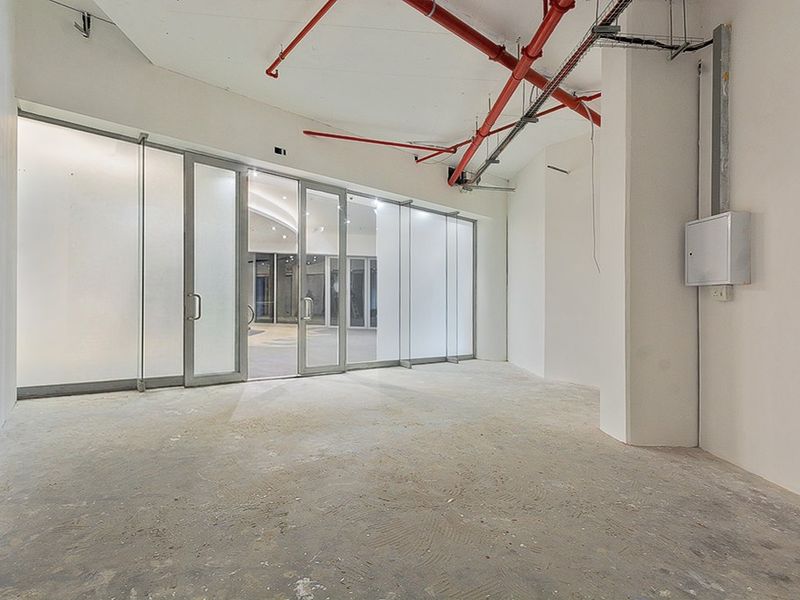 An empty commercial office space featuring frosted glass partitions, exposed fire sprinkler piping, and unfinished concrete flooring, ready for custom fit-out.