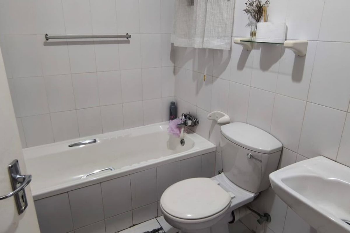 A functional bathroom featuring a bathtub, pedestal basin, and toilet with white wall tiling throughout.