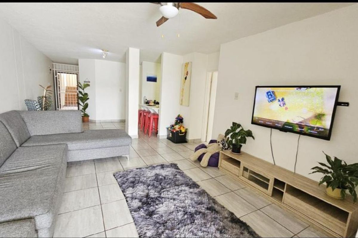 Open plan living area featuring tiled flooring, a ceiling fan, and a breakfast bar connecting to the kitchen space.