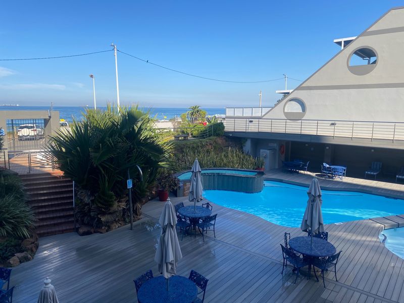 A well-maintained outdoor pool area featuring timber decking, a swimming pool, and ocean views, providing a relaxing communal space for residents.