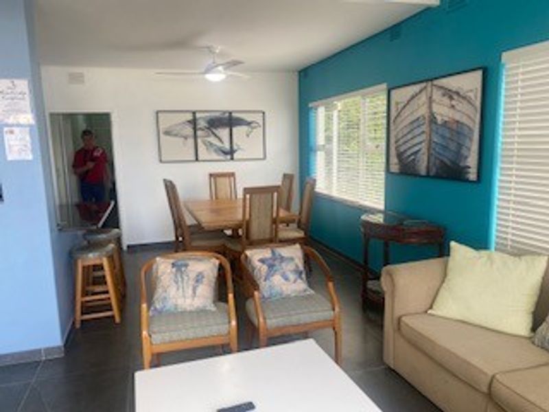 Open plan living and dining area featuring tiled floors, ceiling fan, and large windows with venetian blinds.
