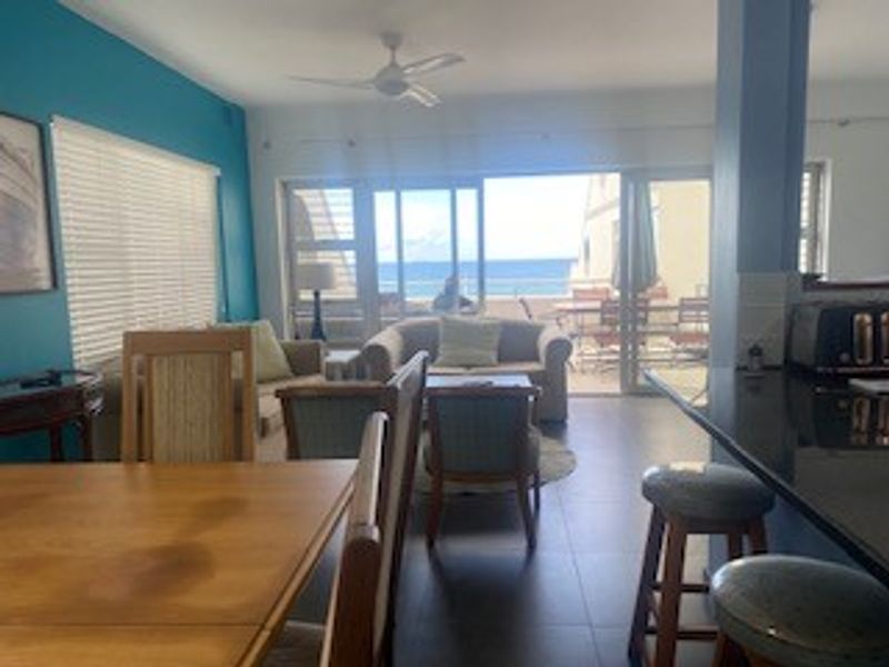 Open-plan living and dining area featuring tiled floors, a breakfast bar with granite countertops, and sliding glass doors leading to a balcony with ocean views.