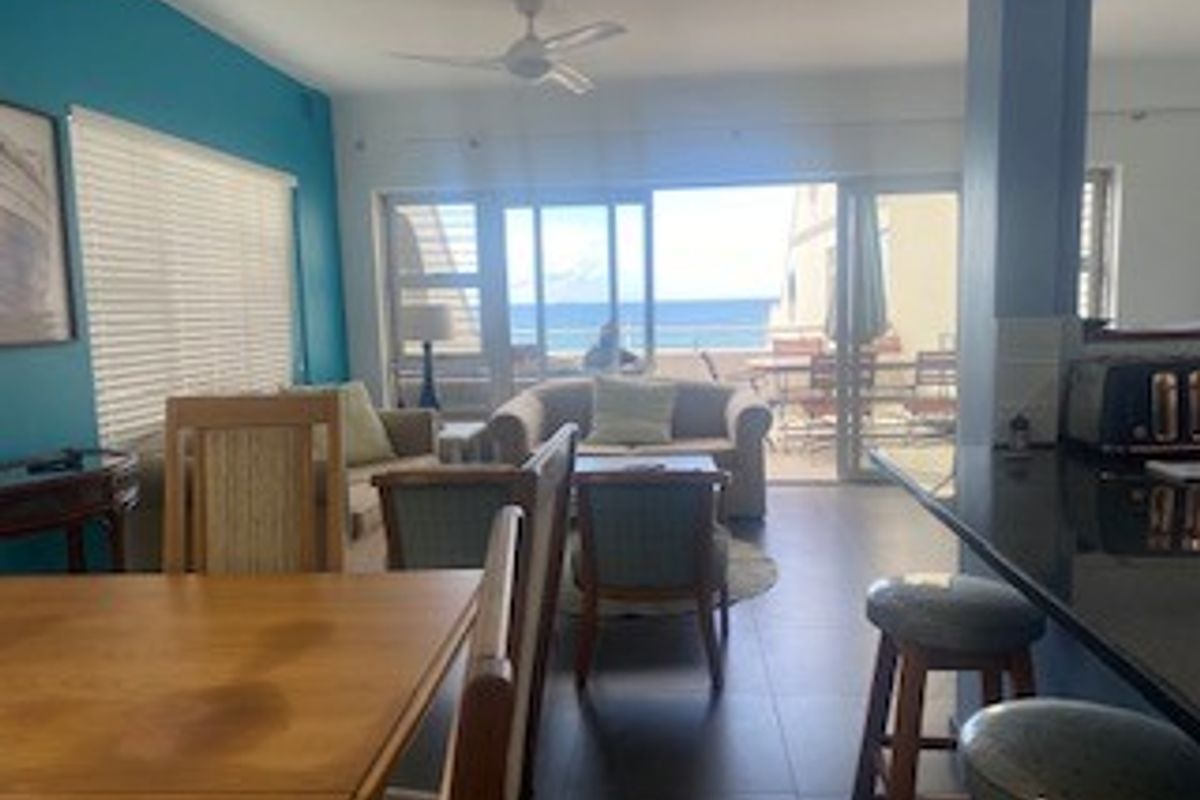 Open-plan living and dining area featuring tiled floors, a breakfast bar with granite countertops, and sliding glass doors leading to a balcony with ocean views.