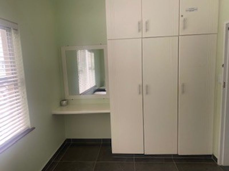 A bedroom featuring built-in cupboards, a vanity area with a mirror, and tiled flooring, providing a functional and clean storage space.