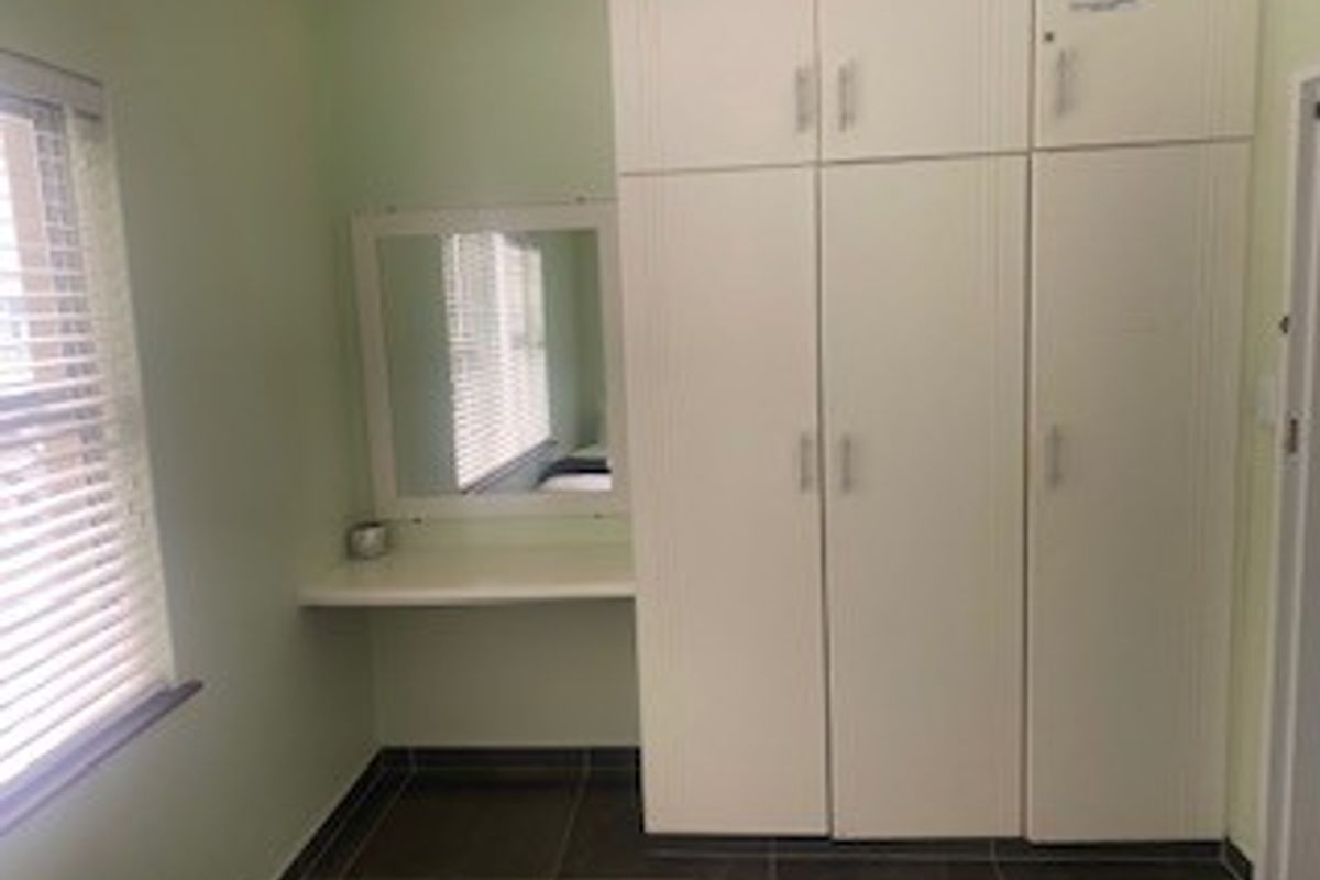 A bedroom featuring built-in cupboards, a vanity area with a mirror, and tiled flooring, providing a functional and clean storage space.
