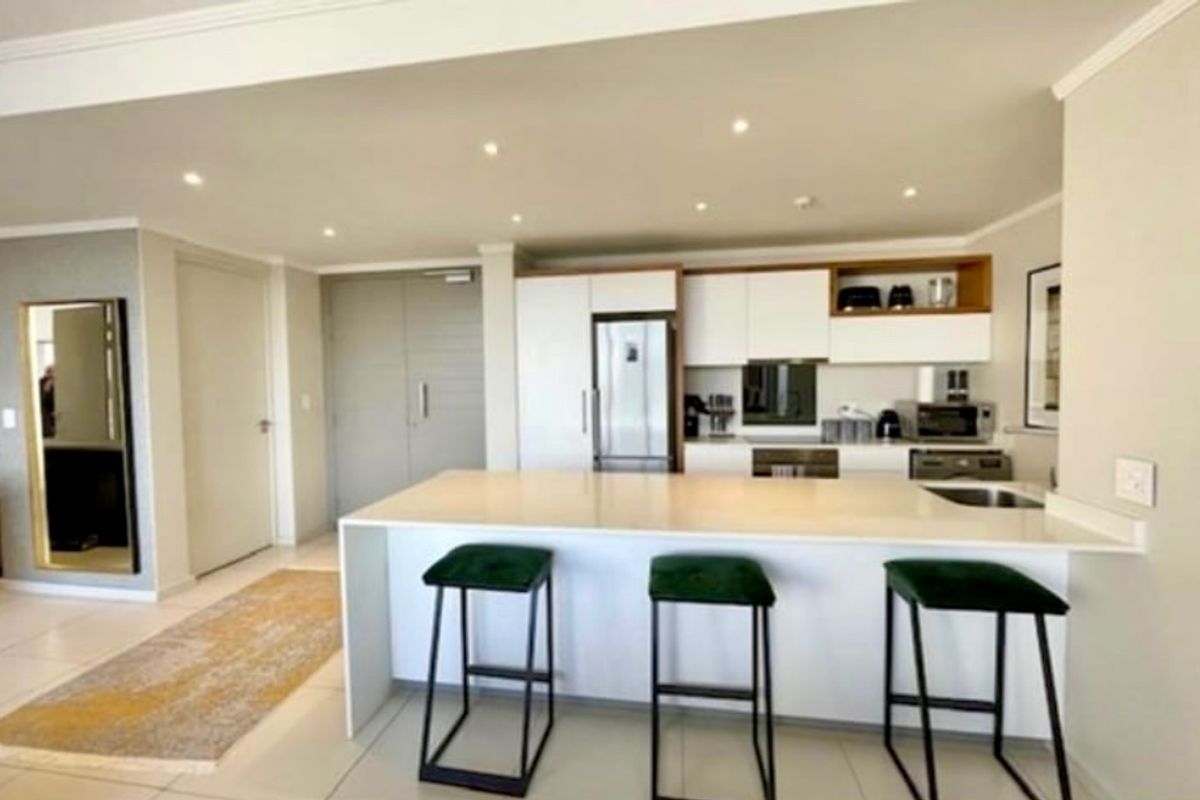 Modern open-plan kitchen featuring a sleek island with quartz countertops, integrated appliances, and clean white cabinetry, seamlessly flowing into the living area.