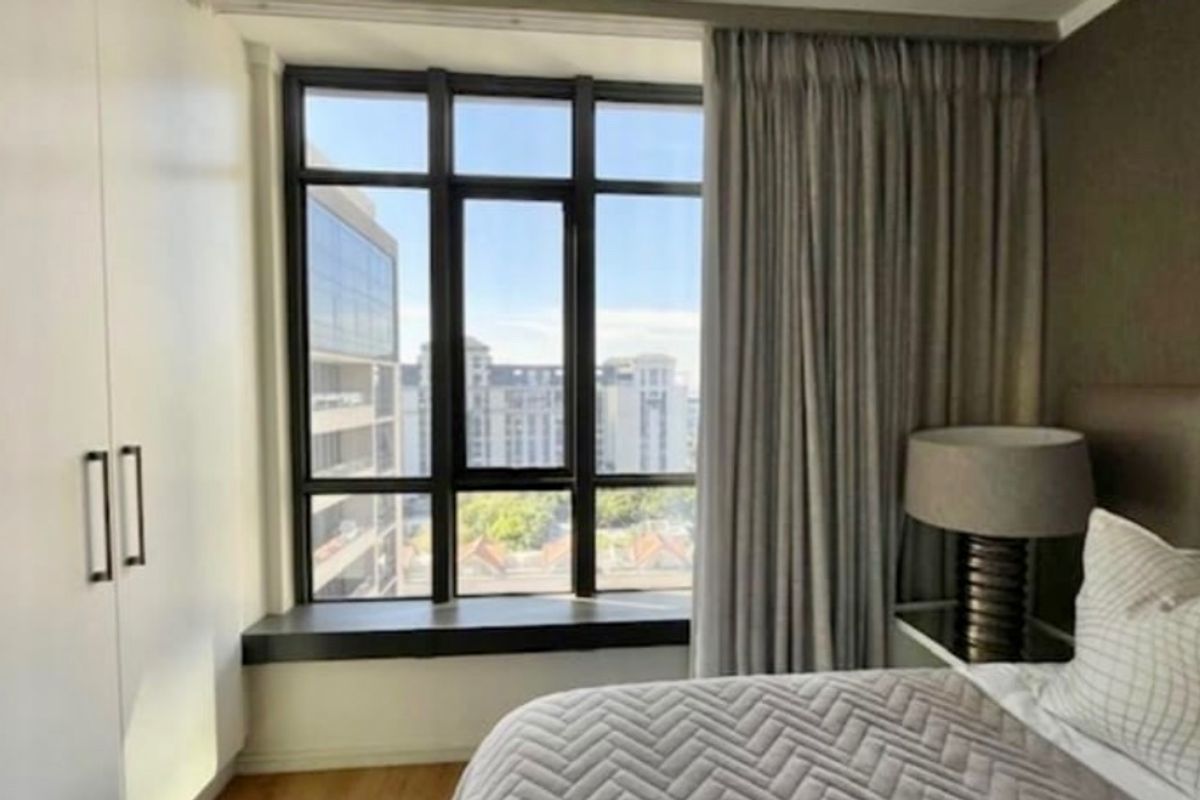 A well-lit bedroom featuring a built-in wardrobe, large window with urban views, and neutral finishes.