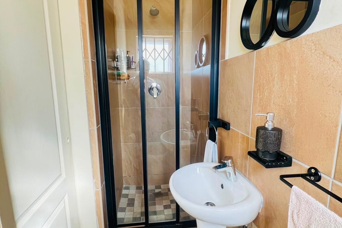A compact bathroom featuring a pedestal basin, a shower enclosure with a black frame, and neutral wall tiling.