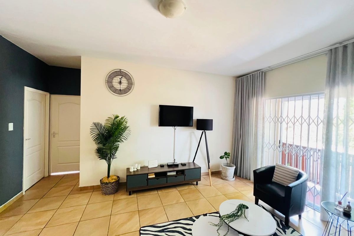 A bright living room featuring tiled flooring, a sliding glass door with security gate, and neutral wall finishes.