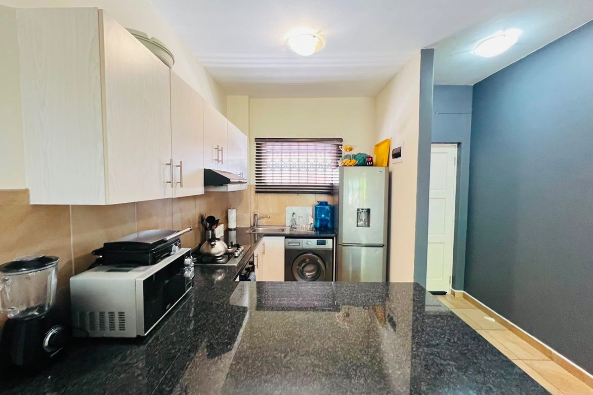 A functional kitchen featuring dark granite countertops, light-toned cabinetry, a tiled backsplash, and integrated laundry plumbing, offering a clean and practical workspace.