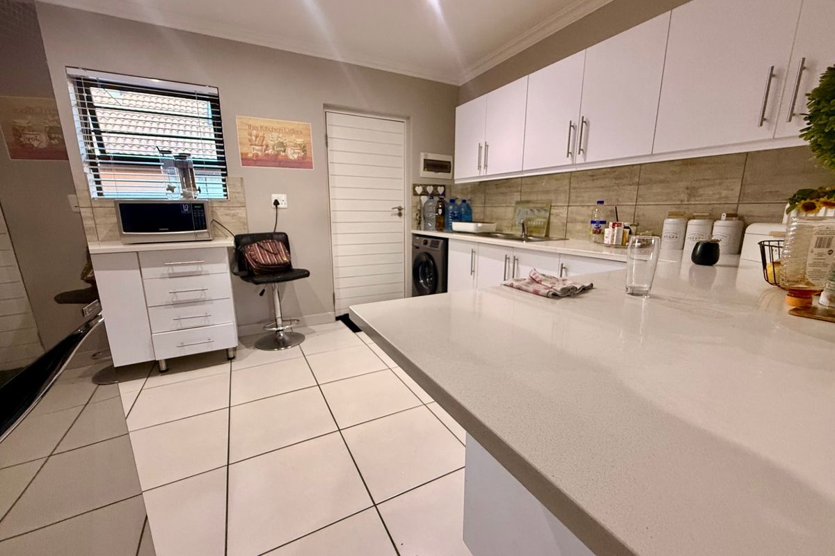 Modern kitchen featuring white cabinetry, stone countertops, tiled backsplash, and integrated laundry facilities with clean tiled flooring and recessed lighting.
