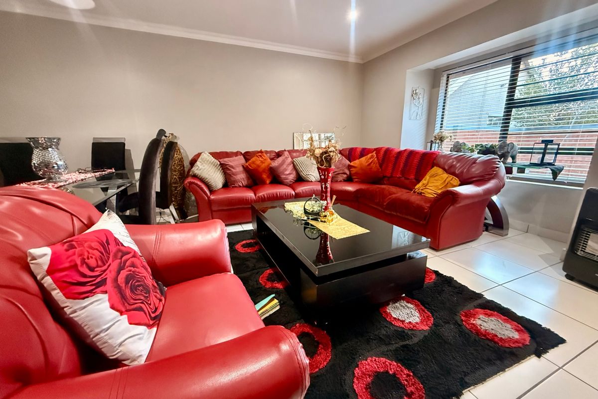 A spacious living room featuring neutral wall tones, tiled flooring, and large windows with venetian blinds, providing a bright and functional living space.