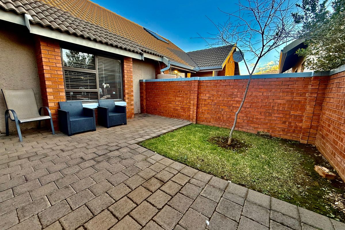 A private rear courtyard featuring a paved patio area, a small lawn, and a brick boundary wall, accessible via a sliding glass door.