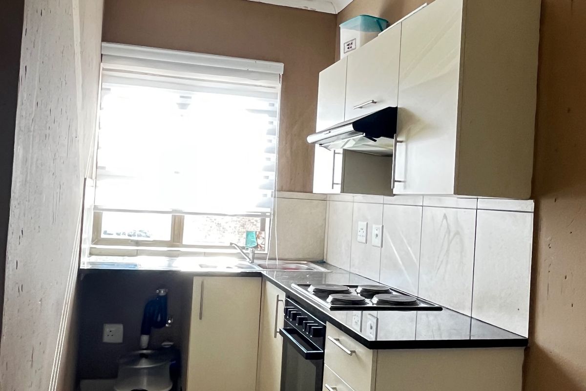 Compact kitchen featuring built-in cabinetry, electric hob, oven, and extractor fan. The space requires wall finishing and minor plumbing maintenance to complete.