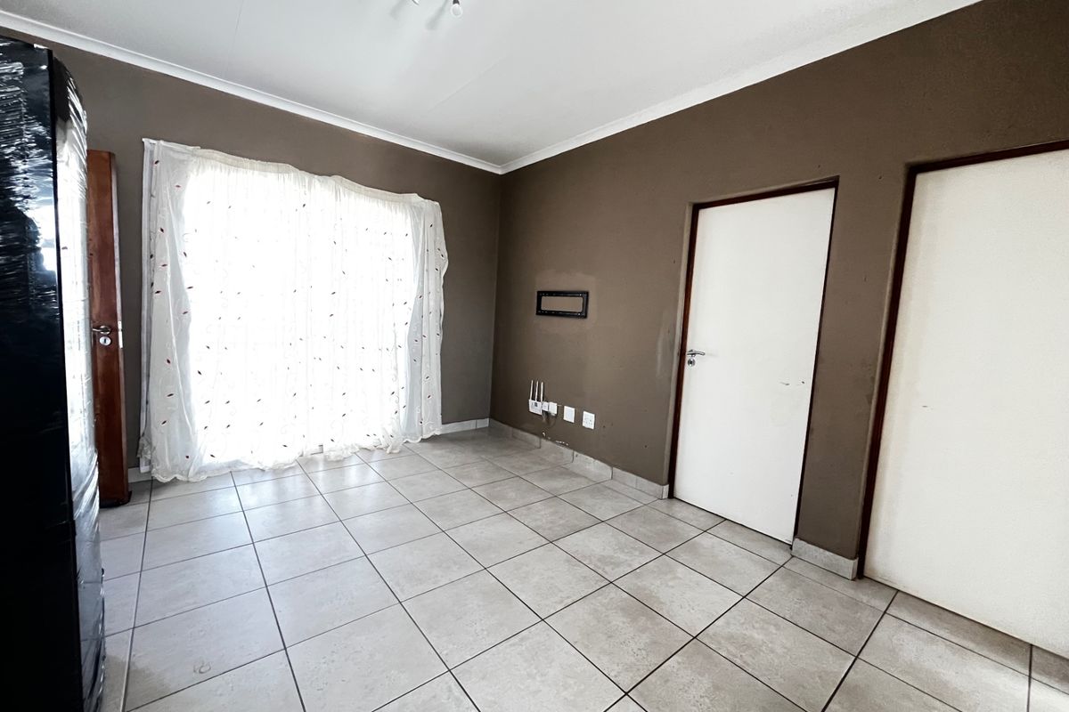 An empty living room featuring neutral ceramic floor tiles, dark brown painted walls, and direct access to a balcony through sliding glass doors.