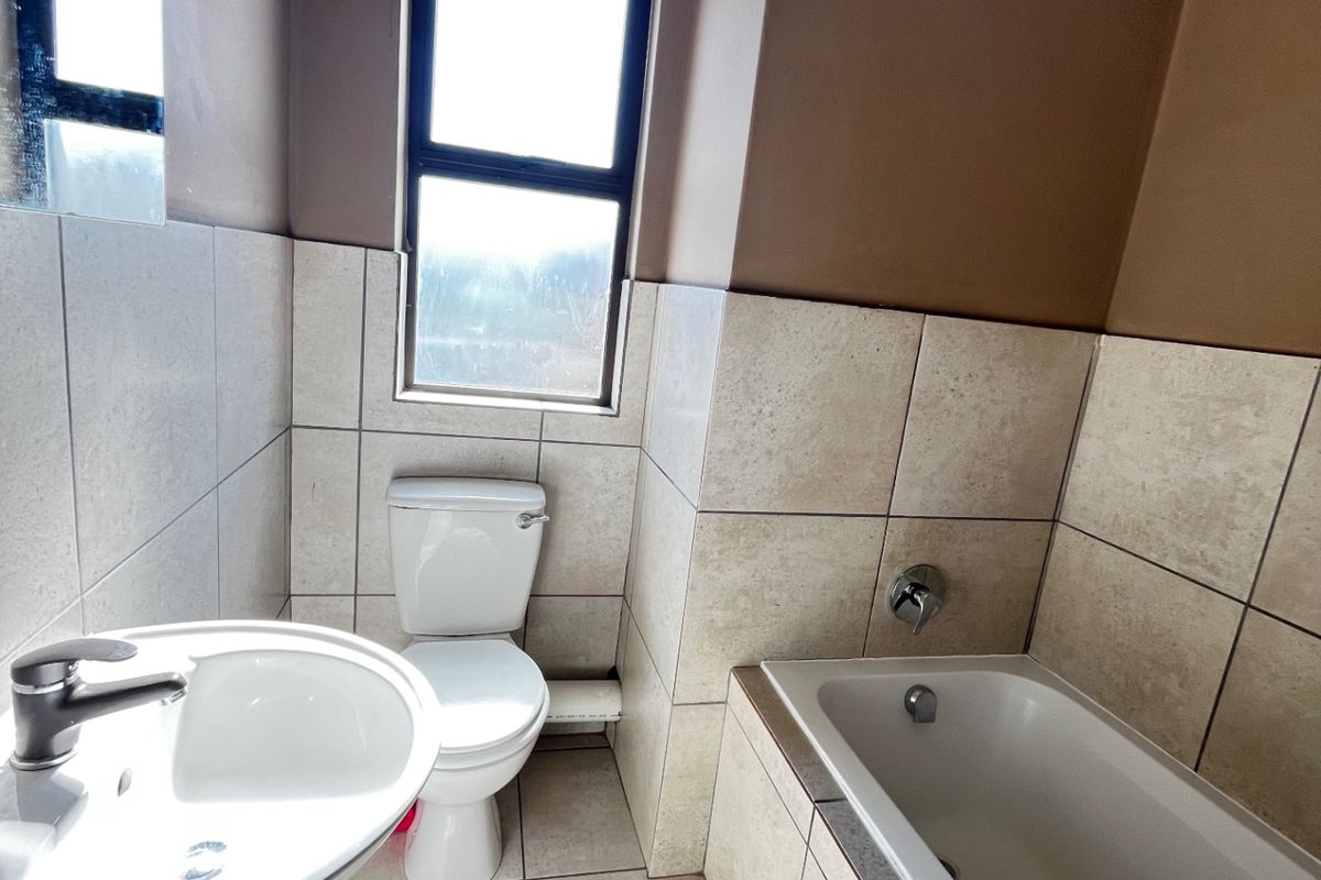 A functional bathroom featuring a pedestal basin, toilet, and built-in bathtub with neutral wall and floor tiling.