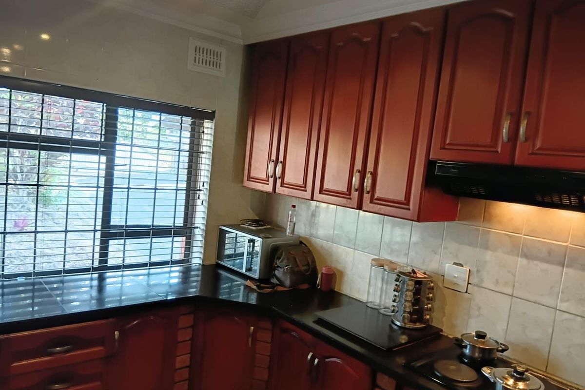 A functional kitchen featuring dark wood cabinetry, black granite countertops, a built-in electric hob with extractor fan, and tiled backsplash.