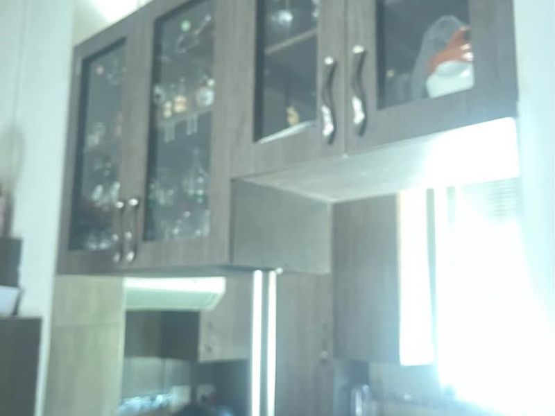 A kitchen area featuring dark wood-toned upper cabinetry with glass inserts, a built-in hob, and a stainless steel support column.