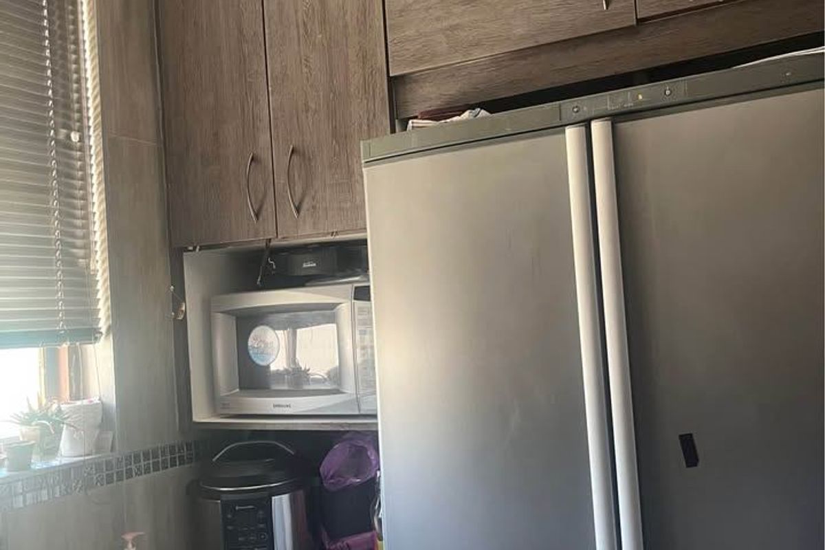 A functional kitchen area featuring wood-look cabinetry, granite countertops, a stainless steel sink, and a built-in microwave space.