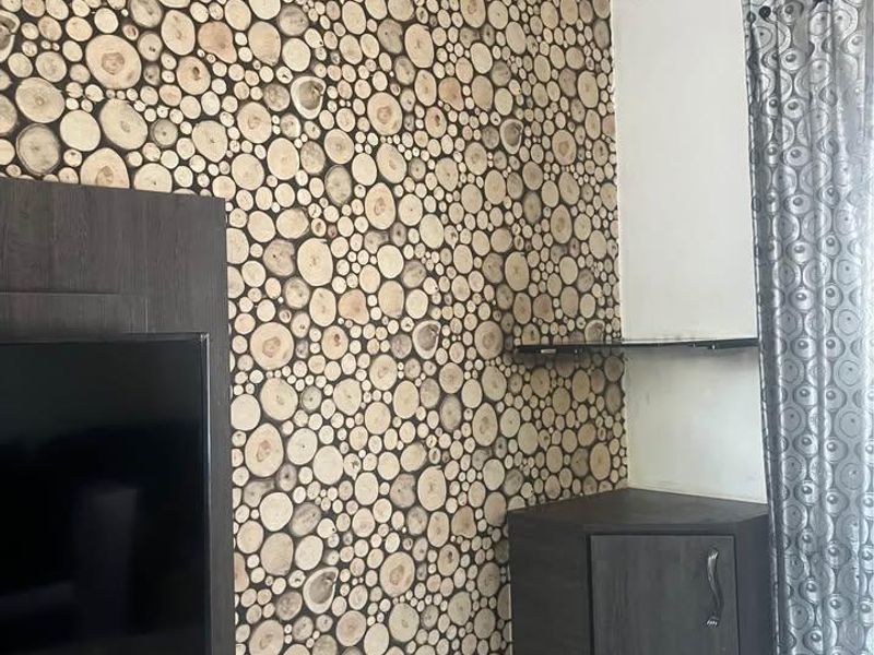 A living room corner featuring a decorative wood slice accent wall, a built-in dark wood corner cabinet, and a floating glass shelf.