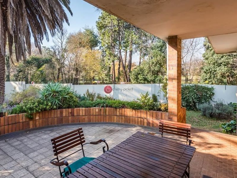 A covered outdoor patio featuring brick structural elements and paved flooring, overlooking a landscaped garden area.