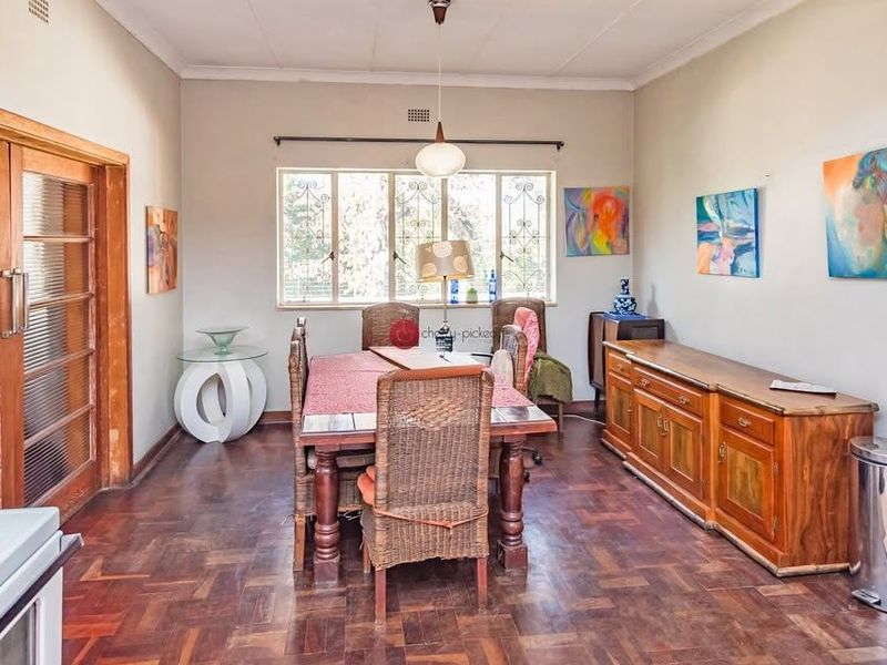 A dining room featuring classic parquet flooring, timber-framed glass doors, and large windows with security bars, offering a traditional and functional space.