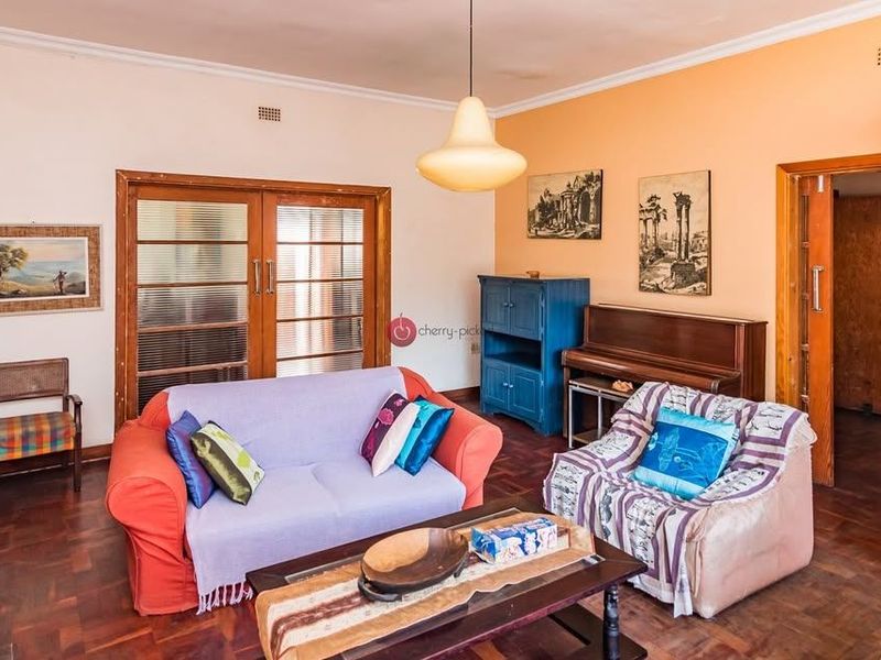A living room featuring classic parquet flooring, timber-framed glass doors, and a central pendant light fixture, offering a warm and traditional aesthetic.